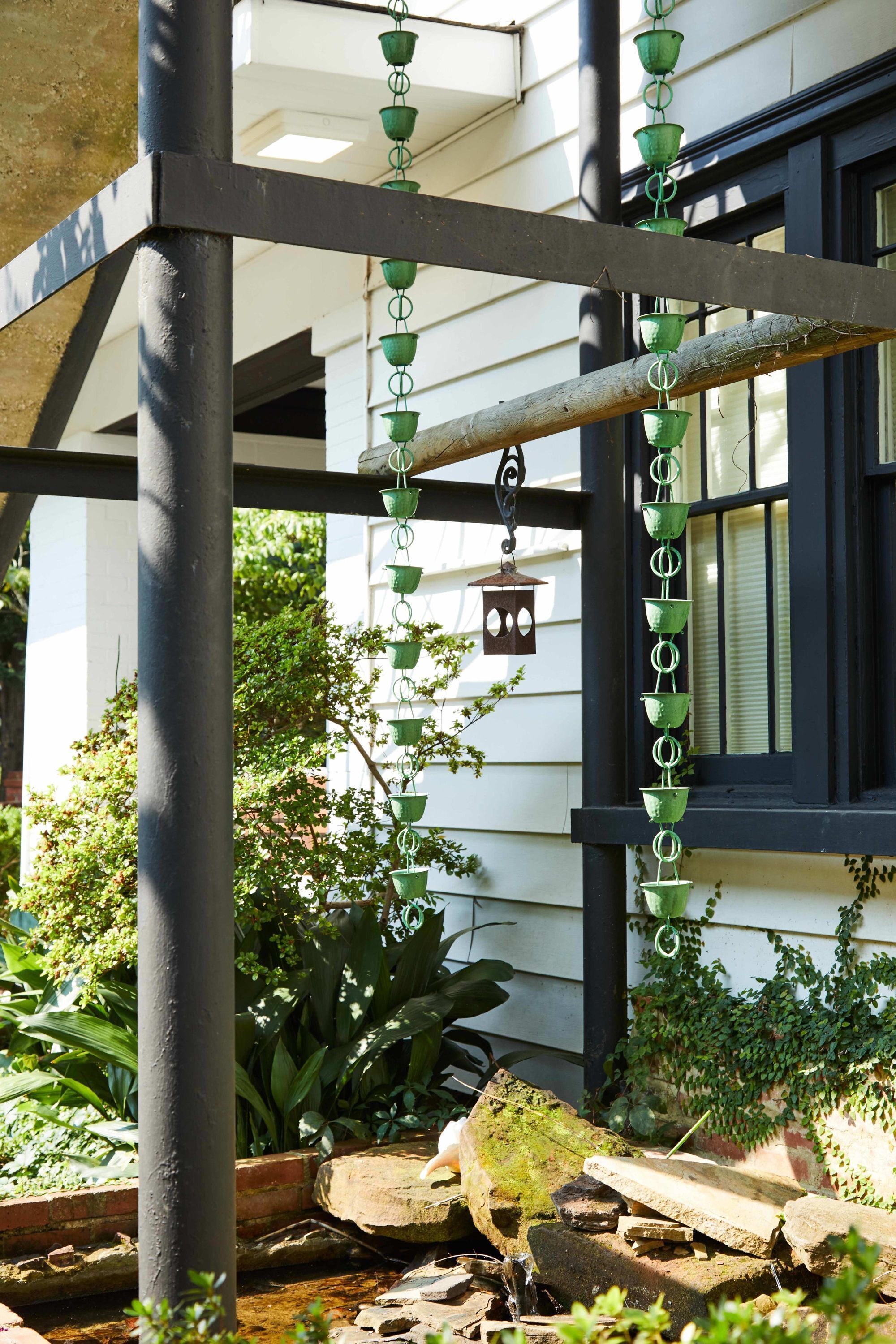 Un espace jardin agrémenté d’une structure métallique servant de support à des jardinières suspendues, d’une bûche en bois et d’une mangeoire à oiseaux.
