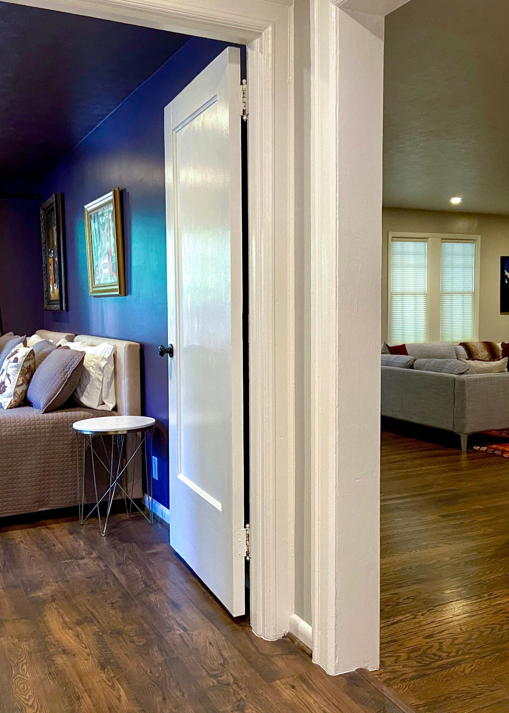 A room with a wooden floor, a white door, a grey sofa, and a small round table.