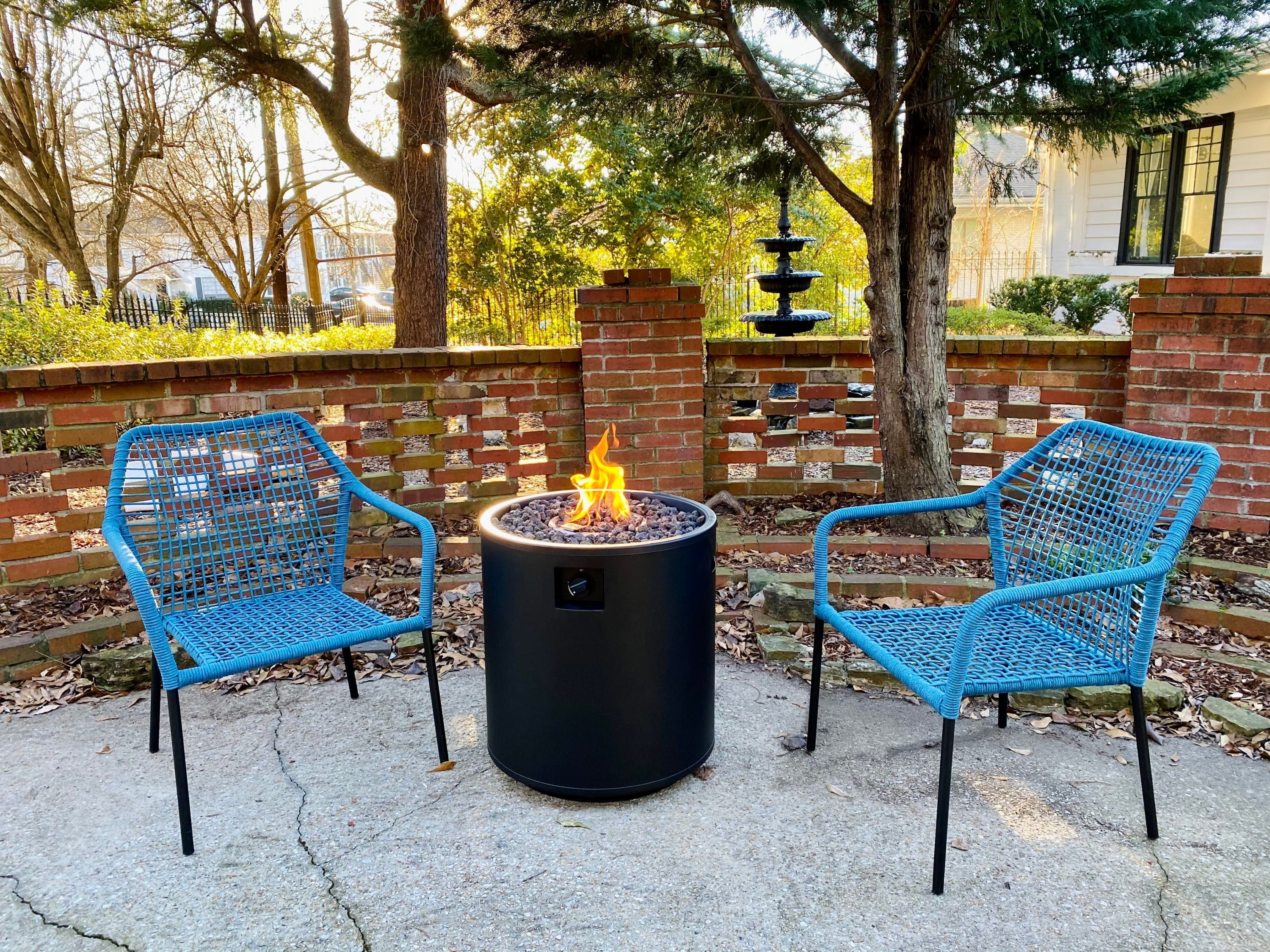 A fire pit with two blue chairs in a brick-walled outdoor area.