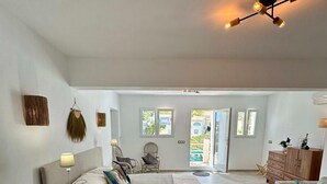 Un dormitorio amplio con una cama grande, mesitas de noche, lámpara de techo y vistas al exterior por una puerta.