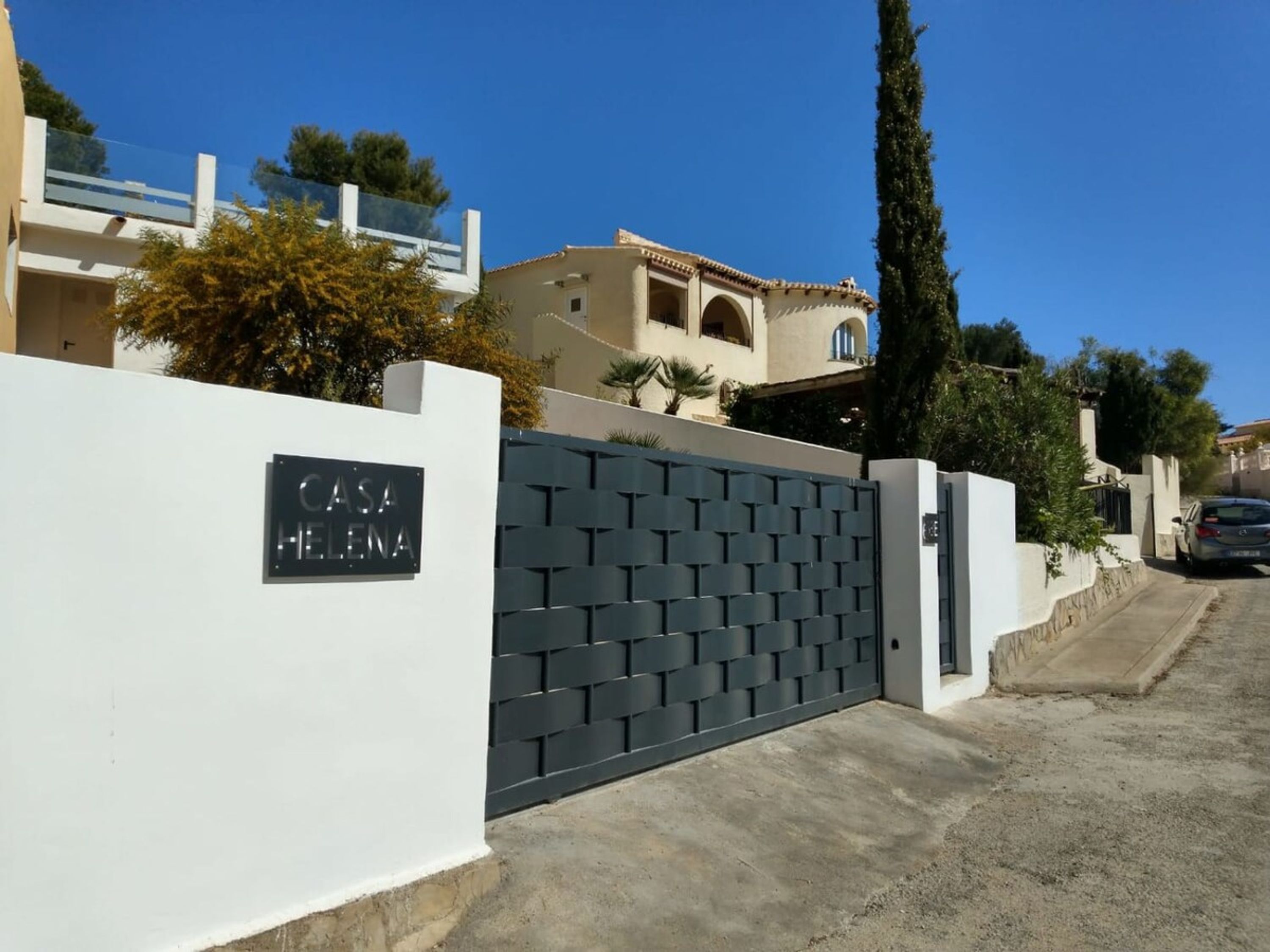 A gated entrance to a residential property named "Casa Helena" with a modern grey gate and a white wall.