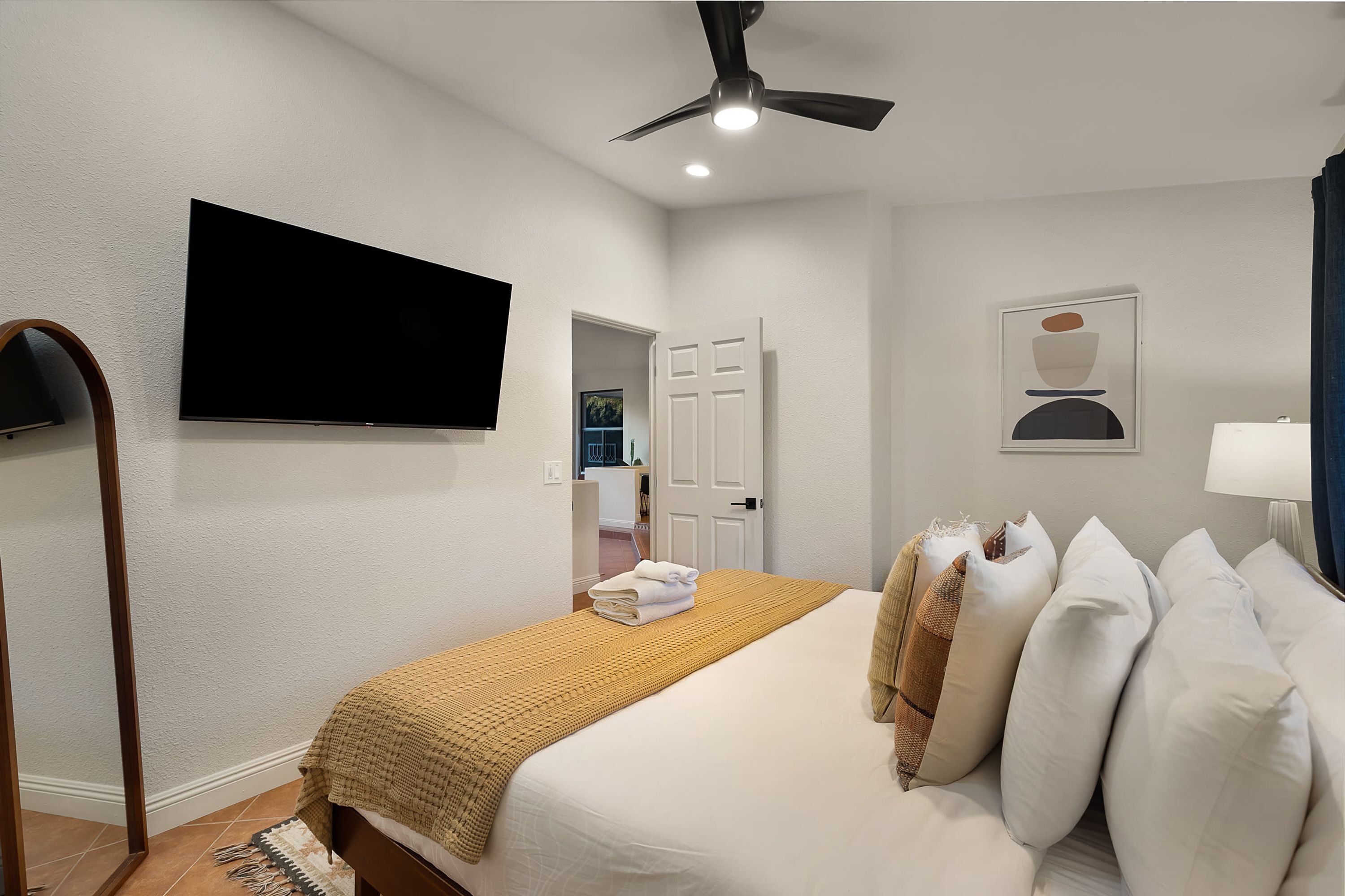A hotel room with a bed, a television, a ceiling fan, a door, and a framed picture on the wall.
