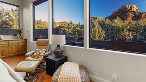 Een moderne woonkamer met een groot raam dat uitzicht biedt op een rotsachtige berg en bomen.