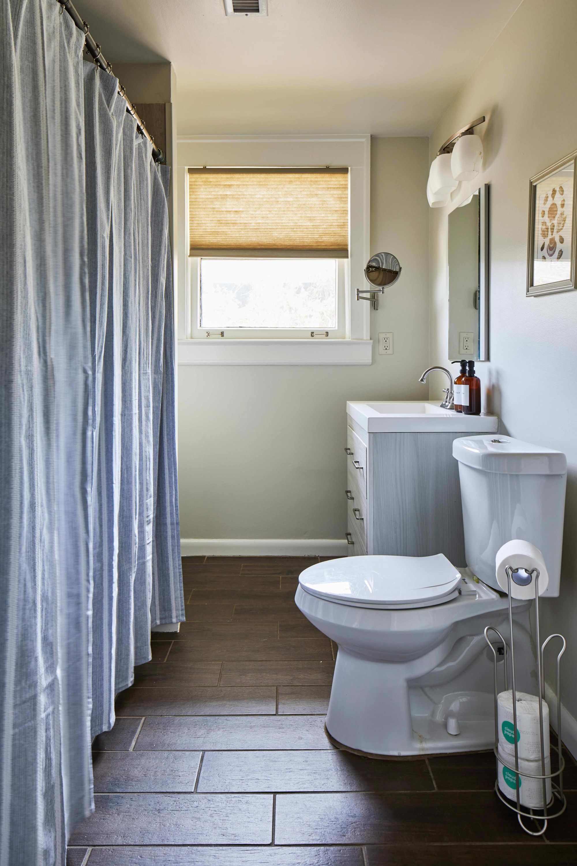 A bathroom with a toilet, a sink, a window with blinds, and a shower curtain.