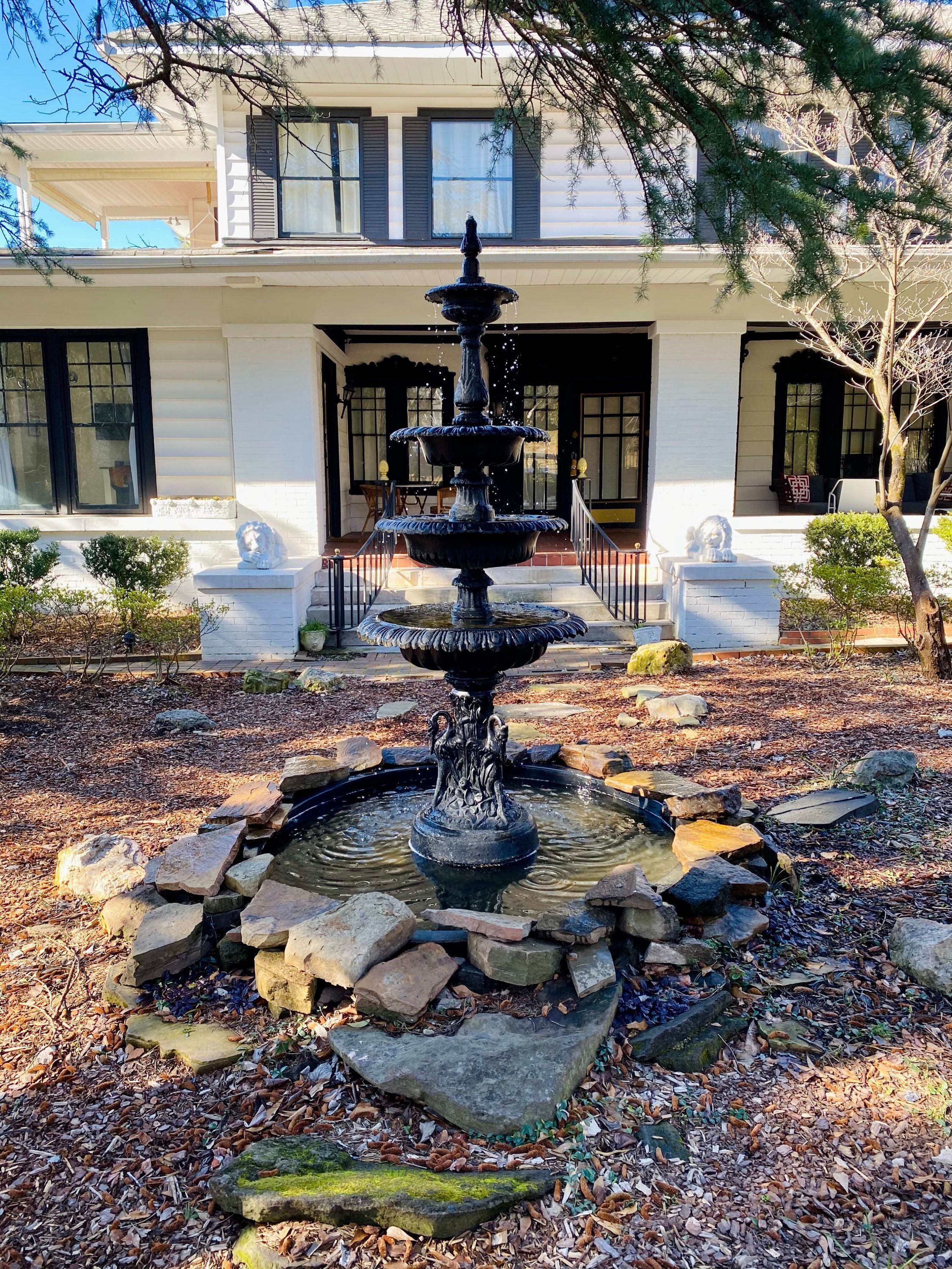 A multi-tiered fountain surrounded by rocks and foliage, with a building in the background.
