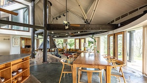 A spacious dining area with a large wooden table and chairs, a stone floor, and large windows offering views of the outdoors. - Belltop Architectural Wonder on Private Mountain (Sevierville)