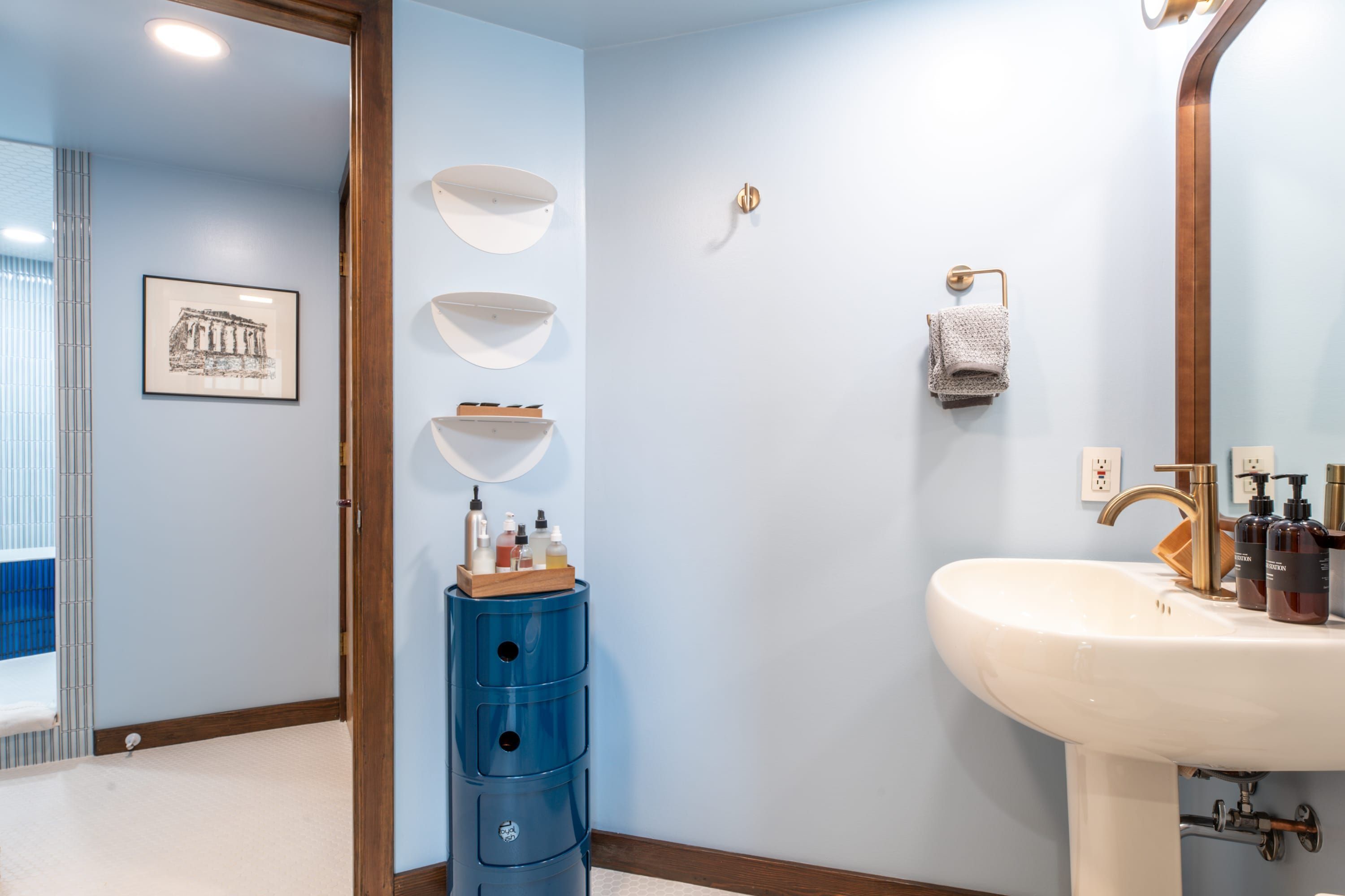 Une salle de bain avec un lavabo blanc, un meuble de rangement bleu et un tableau encadré au mur.