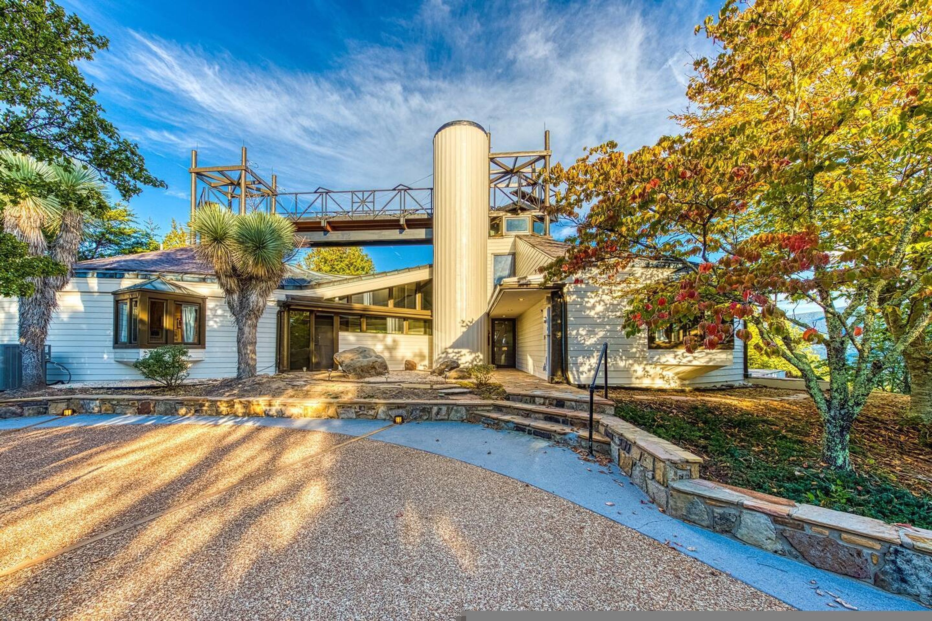 Une maison moderne dotée d’une grande structure cylindrique, d’un patio couvert et d’une allée menant à l’entrée.