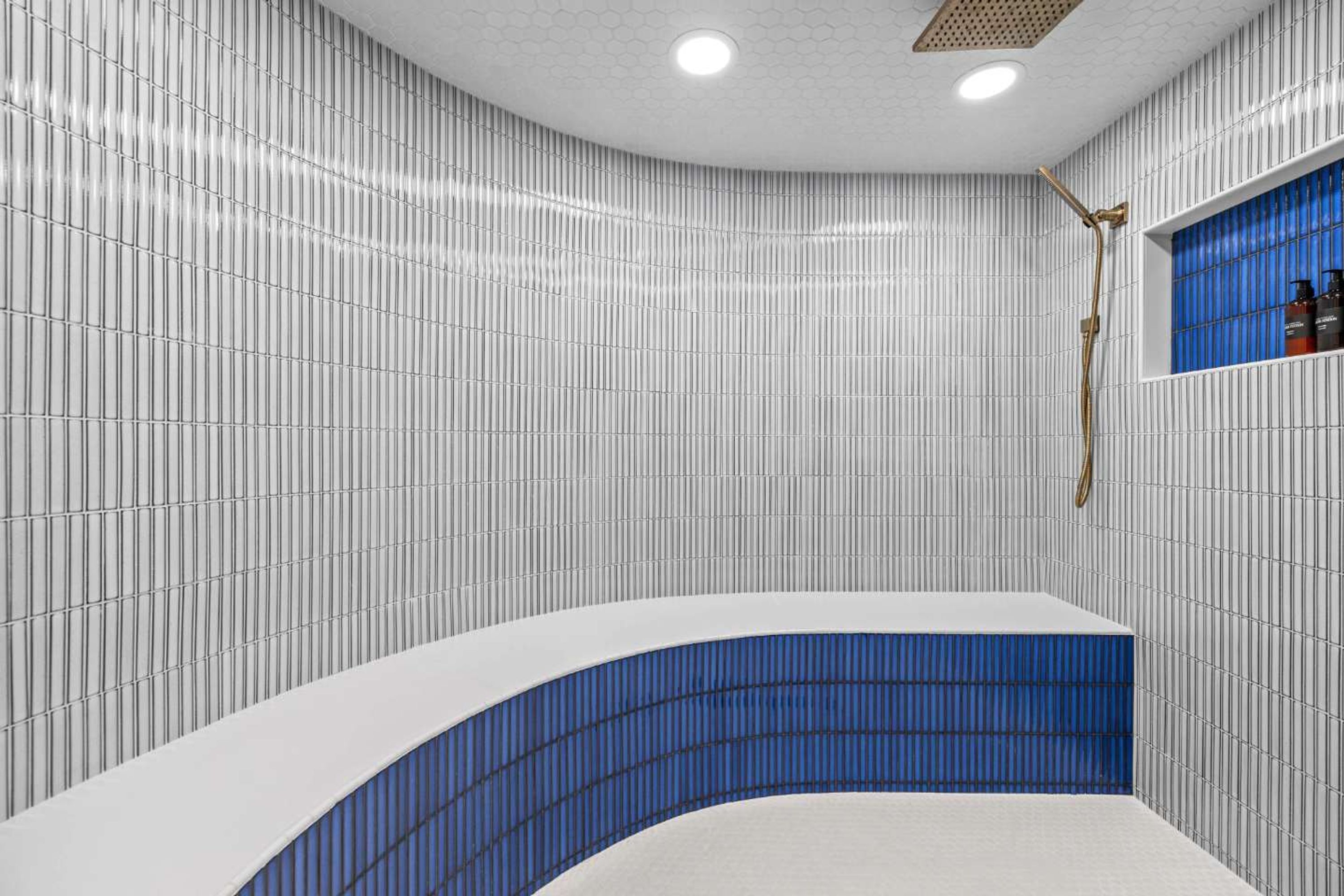 A modern bathroom with vertical striped tiles, a blue-tiled shower area, and a built-in shelf with toiletries.