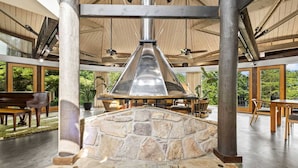 A stone fireplace with a chimney, surrounded by wooden furniture and large windows offering views of greenery. - Belltop Architectural Wonder on Private Mountain (Sevierville)