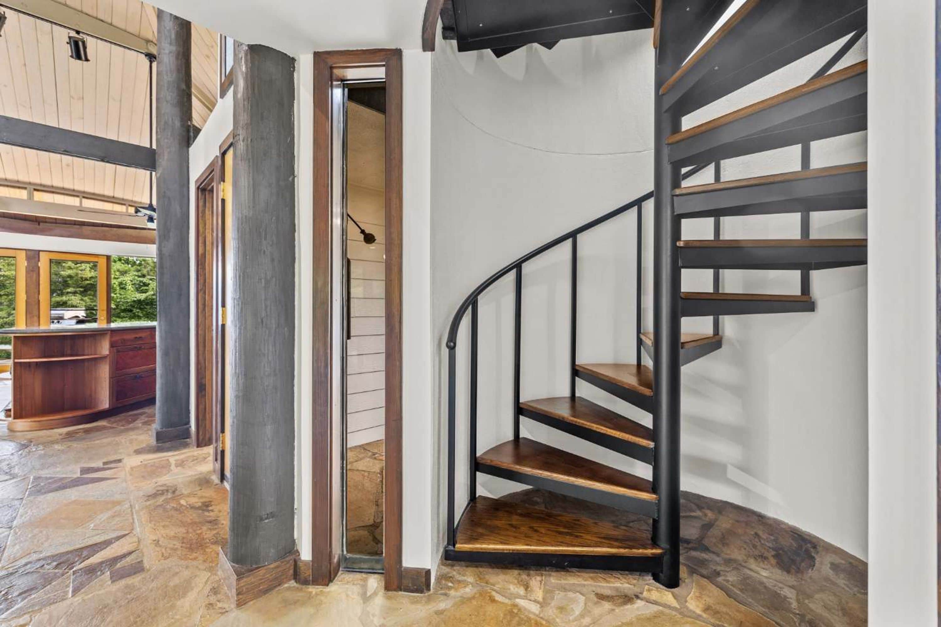 A spiral staircase with wooden steps and metal railings, leading to an upper level.