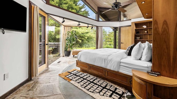 A bedroom with a large bed, wooden headboard, and a ceiling fan. There is a TV mounted on the wall and a window providing a view of the outdoors. - Belltop Architectural Wonder on Private Mountain (Sevierville)
