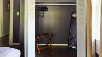 A bedroom with a bed, a wooden floor, a closet with a hanging rack, and a window with curtains.