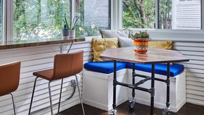 A corner seating area with a table and chairs, large windows with a view of trees, and a hanging light fixture. - Charles on 11th - Beautifully Restored Historic Southside Home Walkable Perfect for Groups (Birmingham)