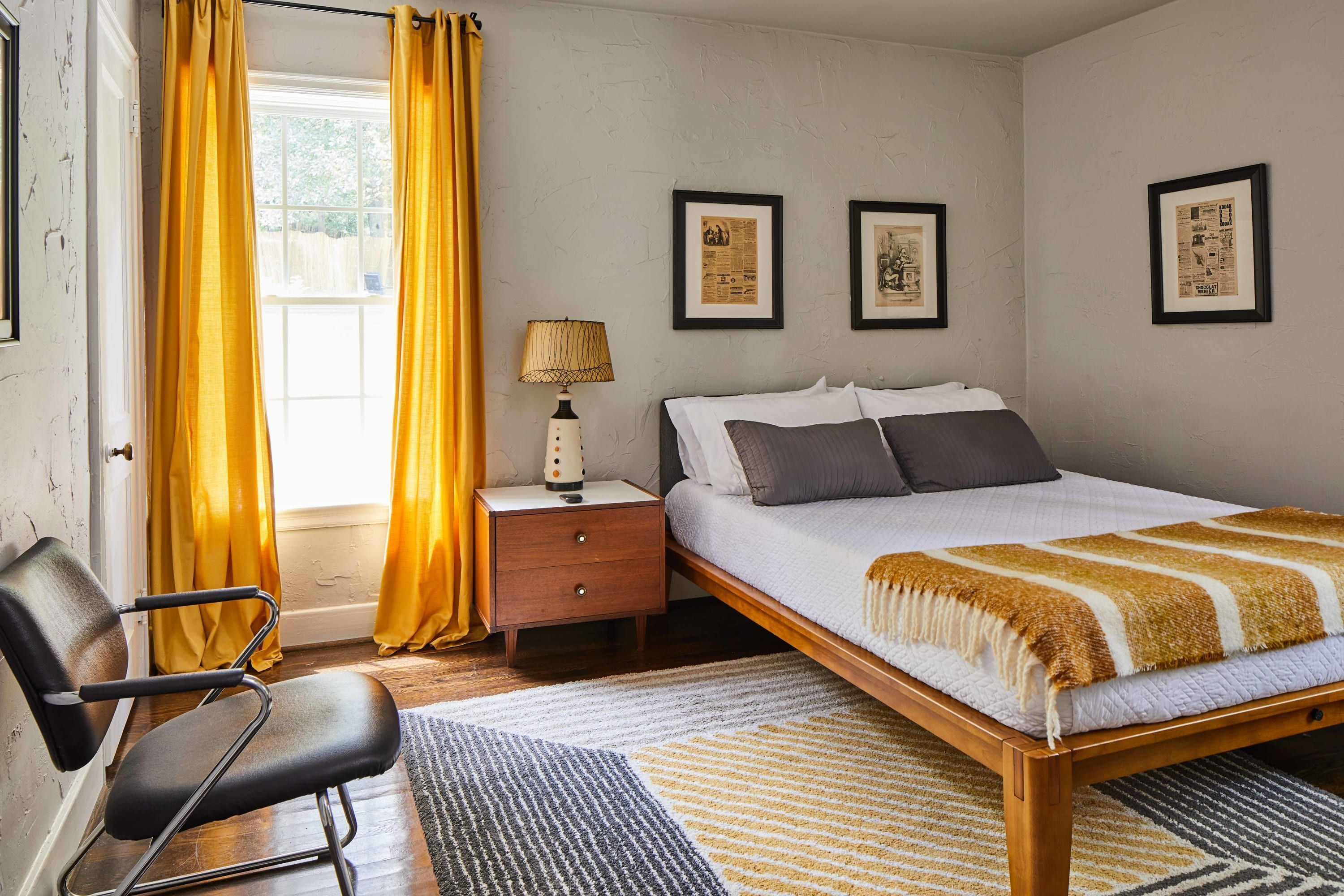 A bedroom with a bed, a chair, a nightstand, and a window with curtains.