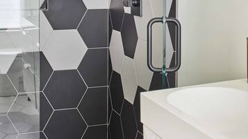 Un baño moderno con ducha, mampara de vidrio y lavamanos blanco.