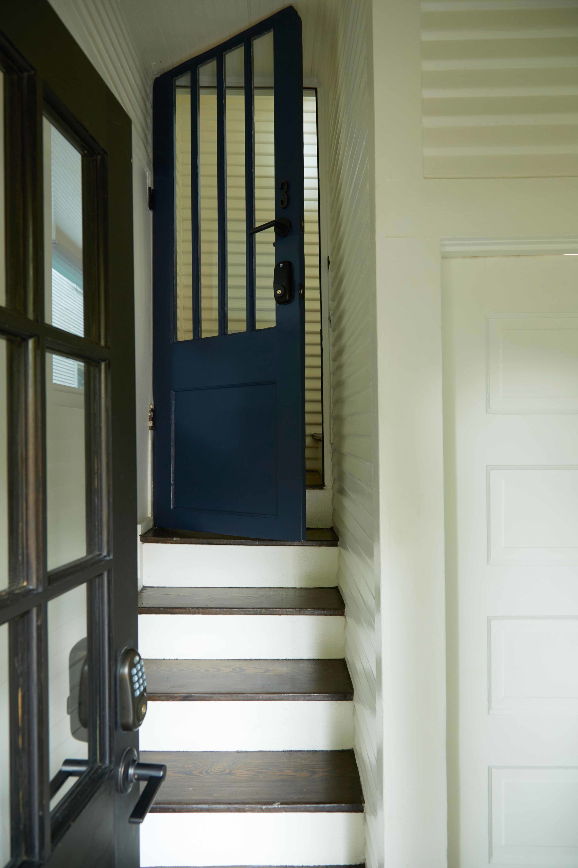 Una escalera que lleva a un umbral con una puerta azul y una blanca.