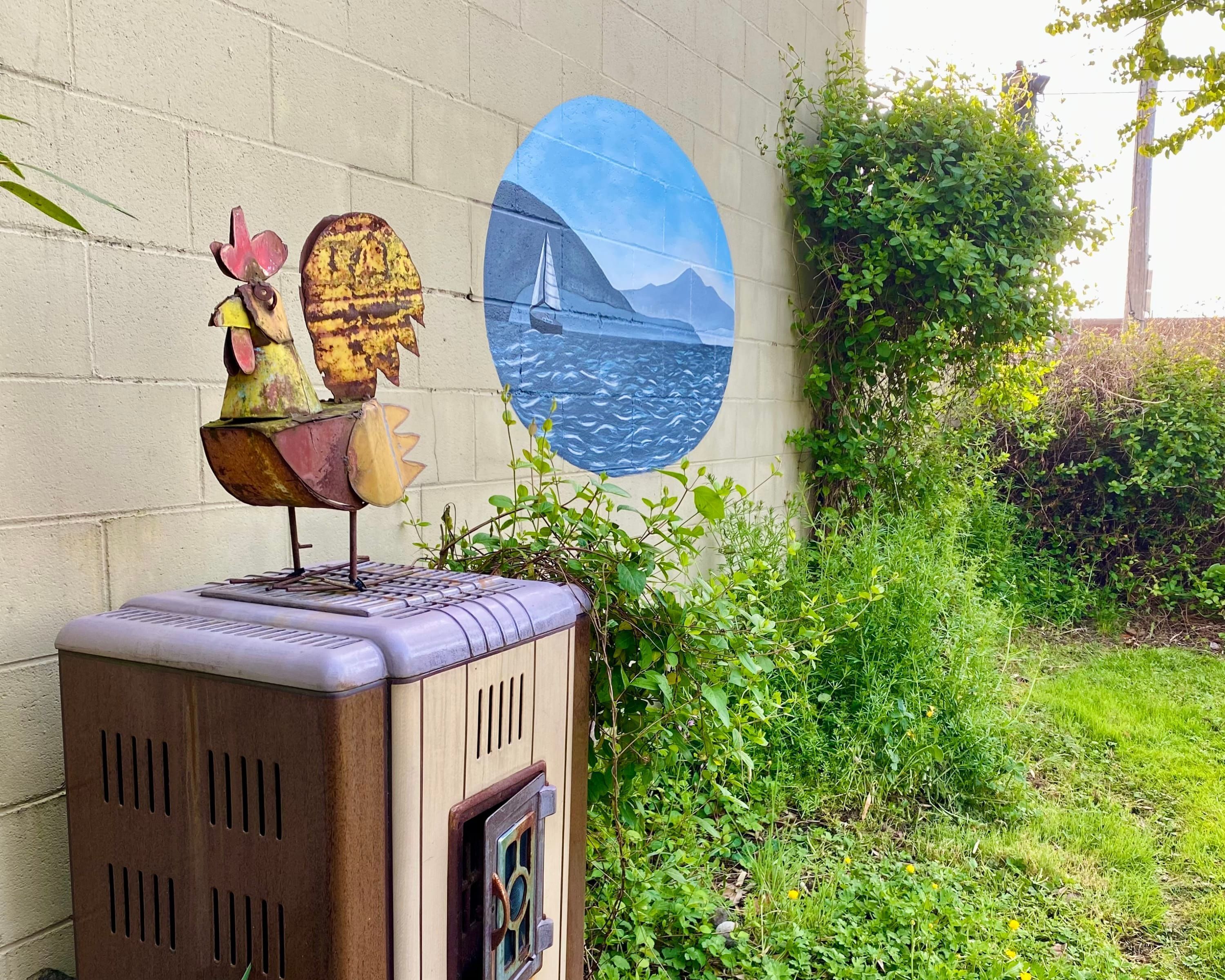 Ein alter Heizkörper im Vintage-Stil mit einem aufgesetzten, dekorativen Hahn, vor einer Wand mit Wandmalerei eines Segelbootes auf dem Wasser.
