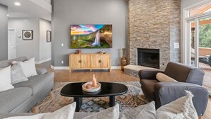 A modern living room with a gray sofa, a brown leather chair, a black coffee table, and a stone fireplace.