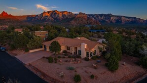 A large house with a spacious patio, surrounded by trees and a view of red rock formations.