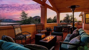 A covered outdoor seating area with a fire feature, chairs, and a view of a lake and mountains.