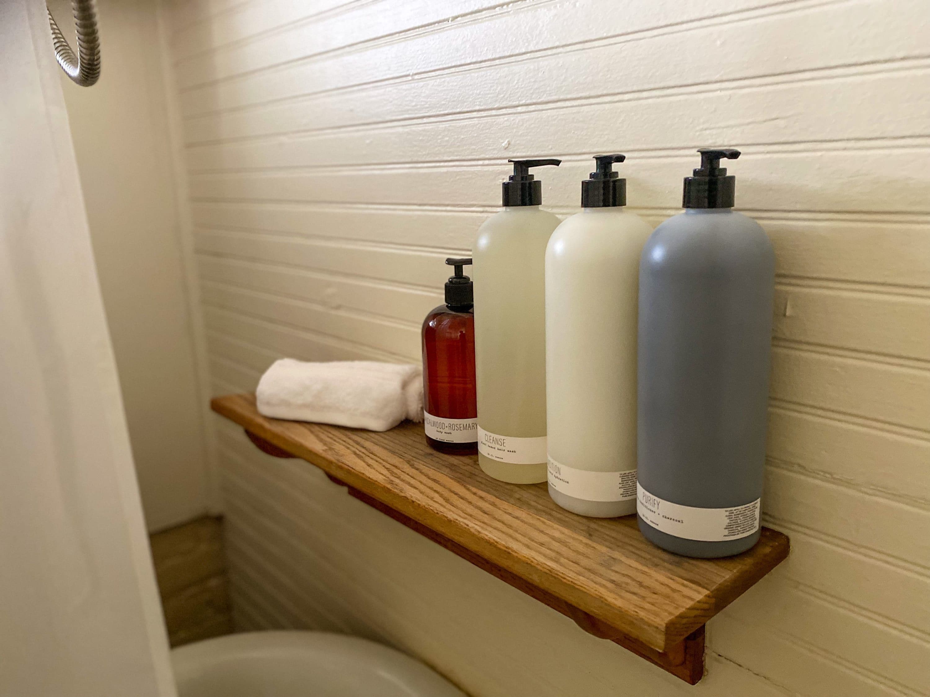A bathroom shelf with four bottles of liquid soap and a white towel.