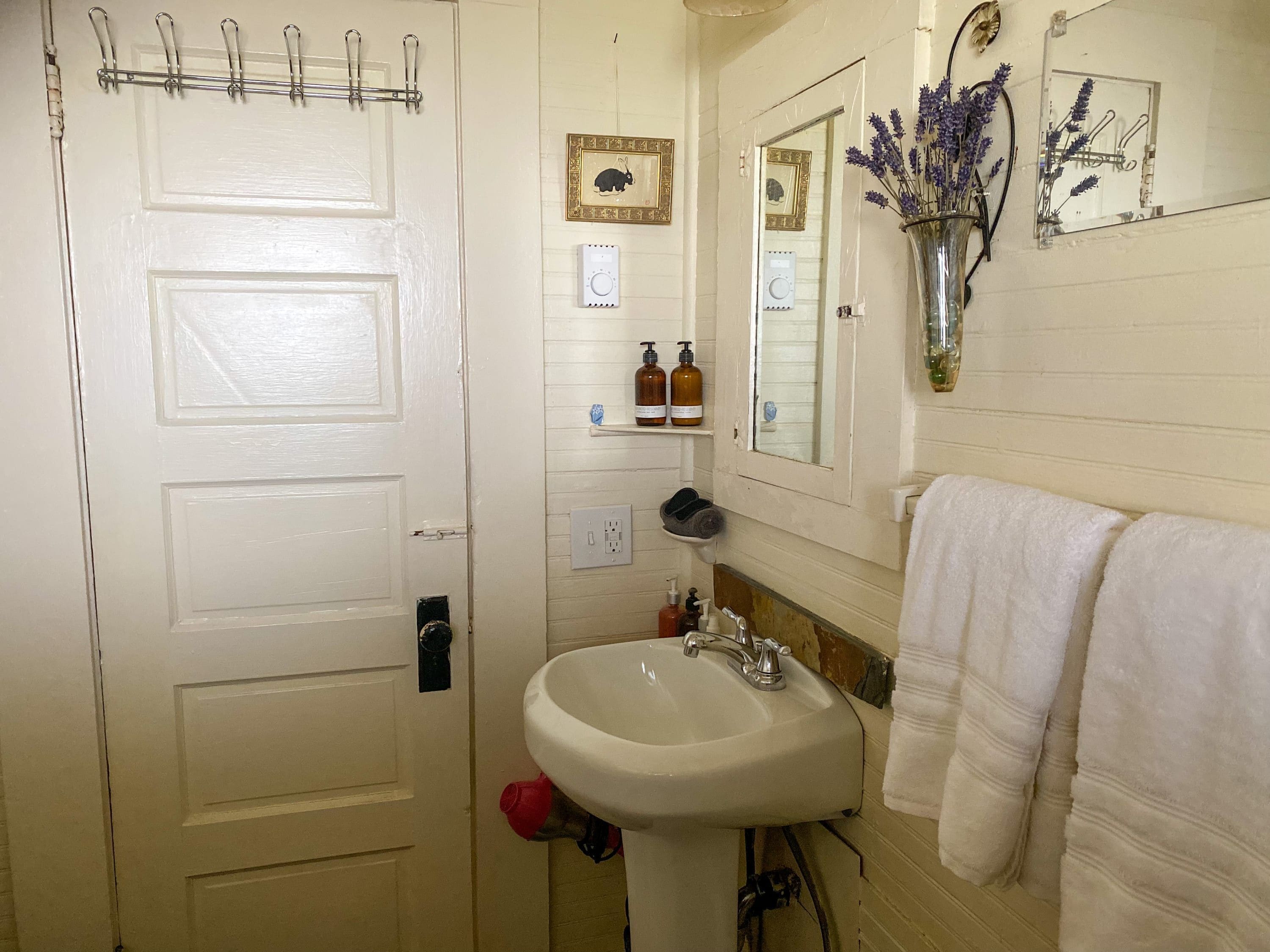 Un baño con una puerta blanca, un lavabo, un espejo y un perchero para toallas.