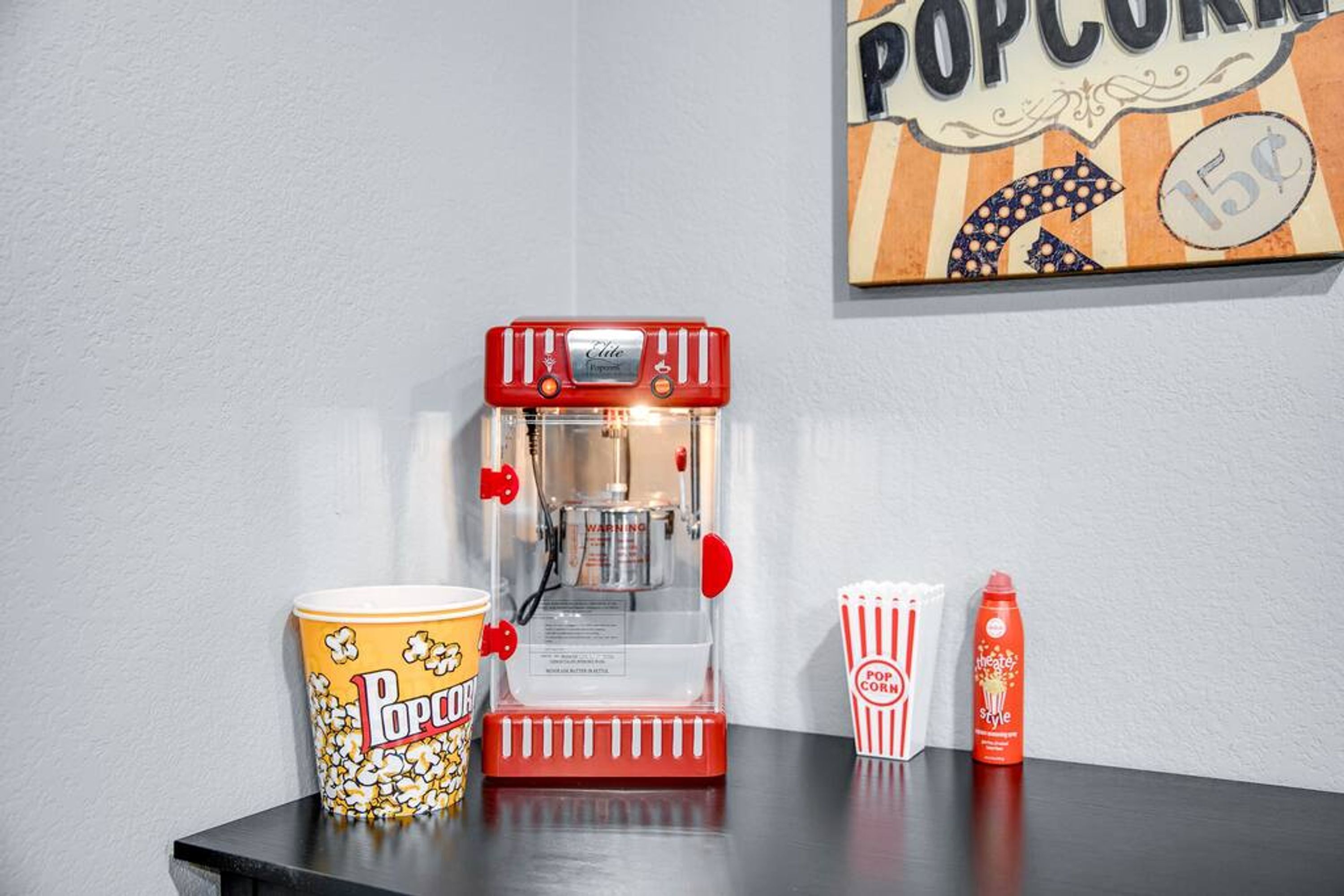 A popcorn machine, a popcorn container, a striped popcorn box, and a bottle of popcorn flavoring on a table.
