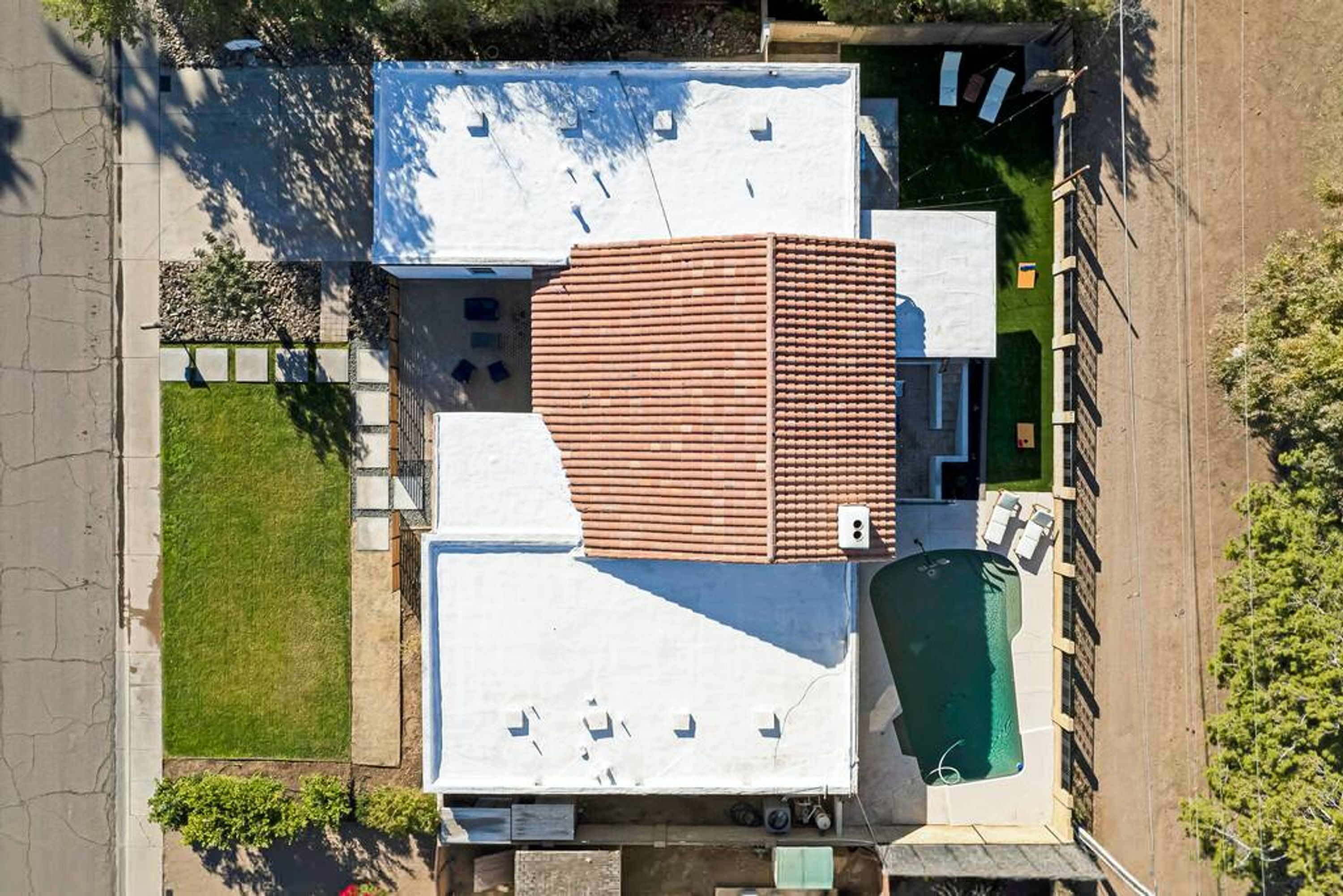 An aerial view of a residential property with a swimming pool, a large tiled roof, and a well-maintained lawn.