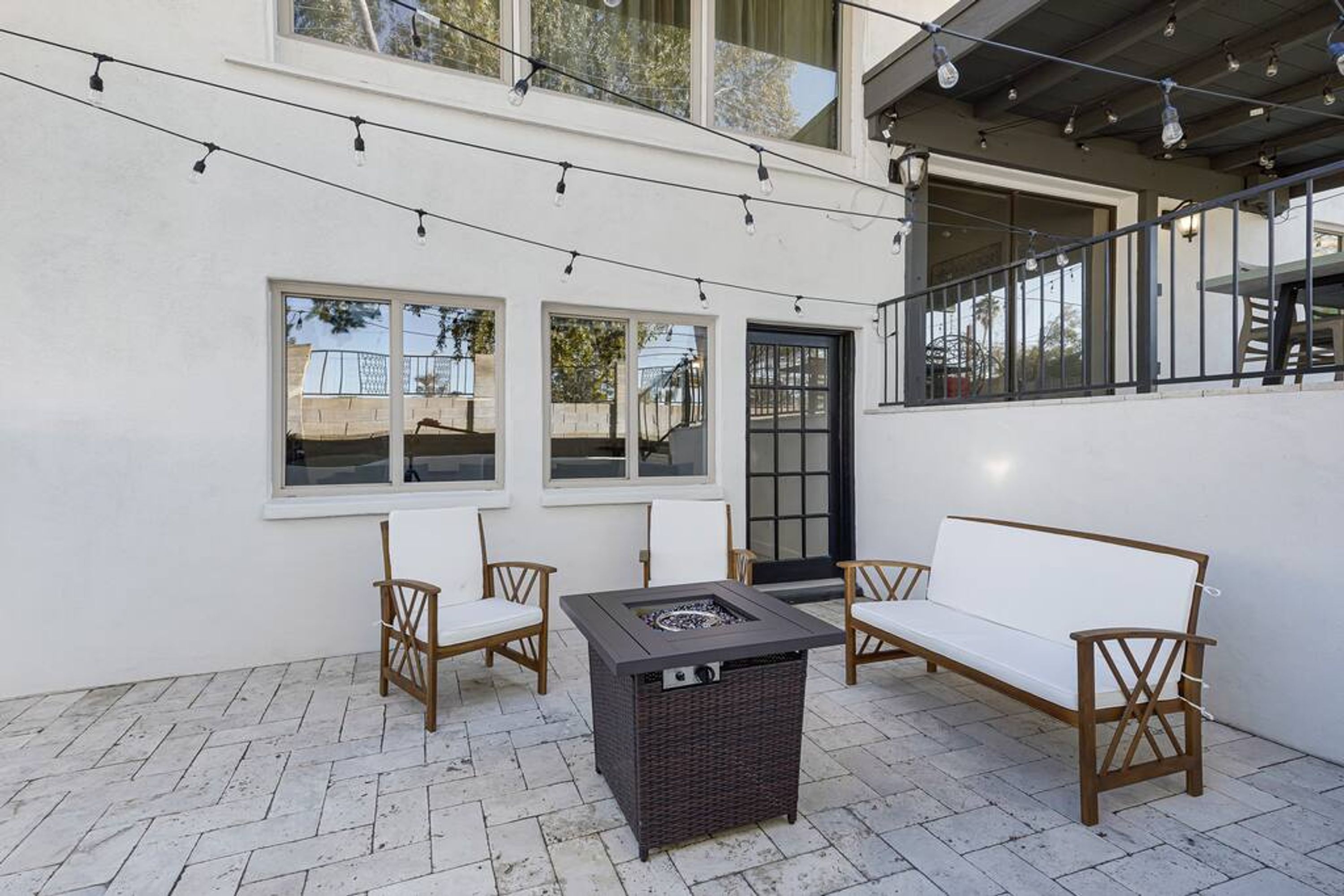 An outdoor patio with a fire pit table, two wooden chairs, and a sofa.