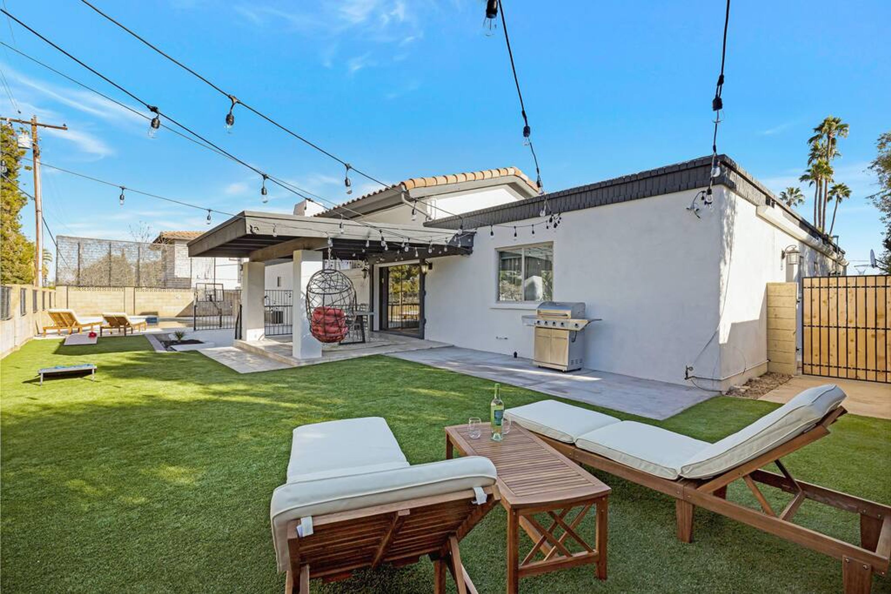Um quintal com área de churrasqueira, espaço para sentar ao ar livre e uma pérgola decorada com luzes.