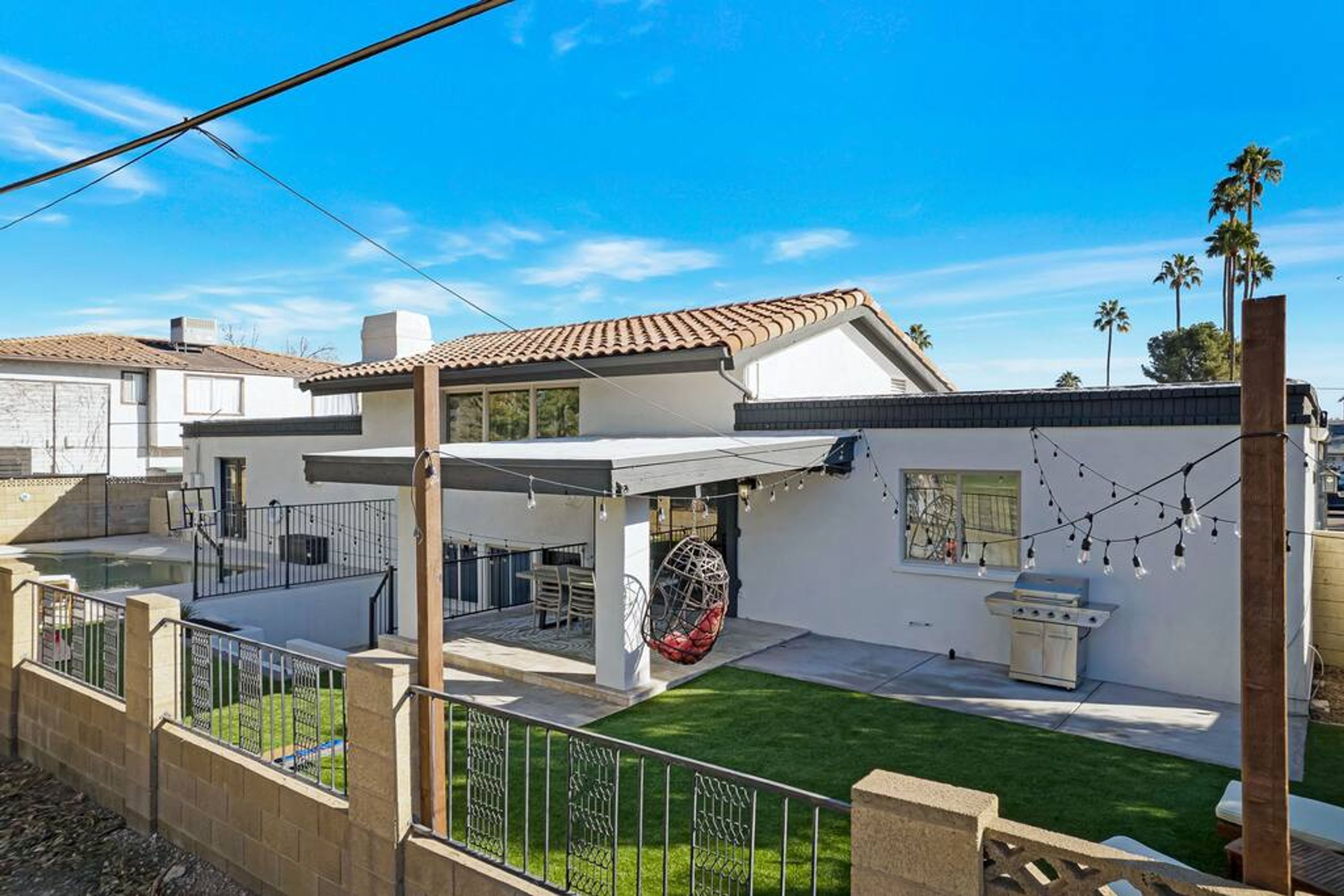 A modern house with a patio, a barbecue grill, and a hanging chair.