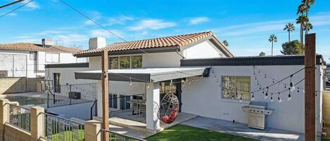 A modern house with a patio, a barbecue grill, and a hanging chair.