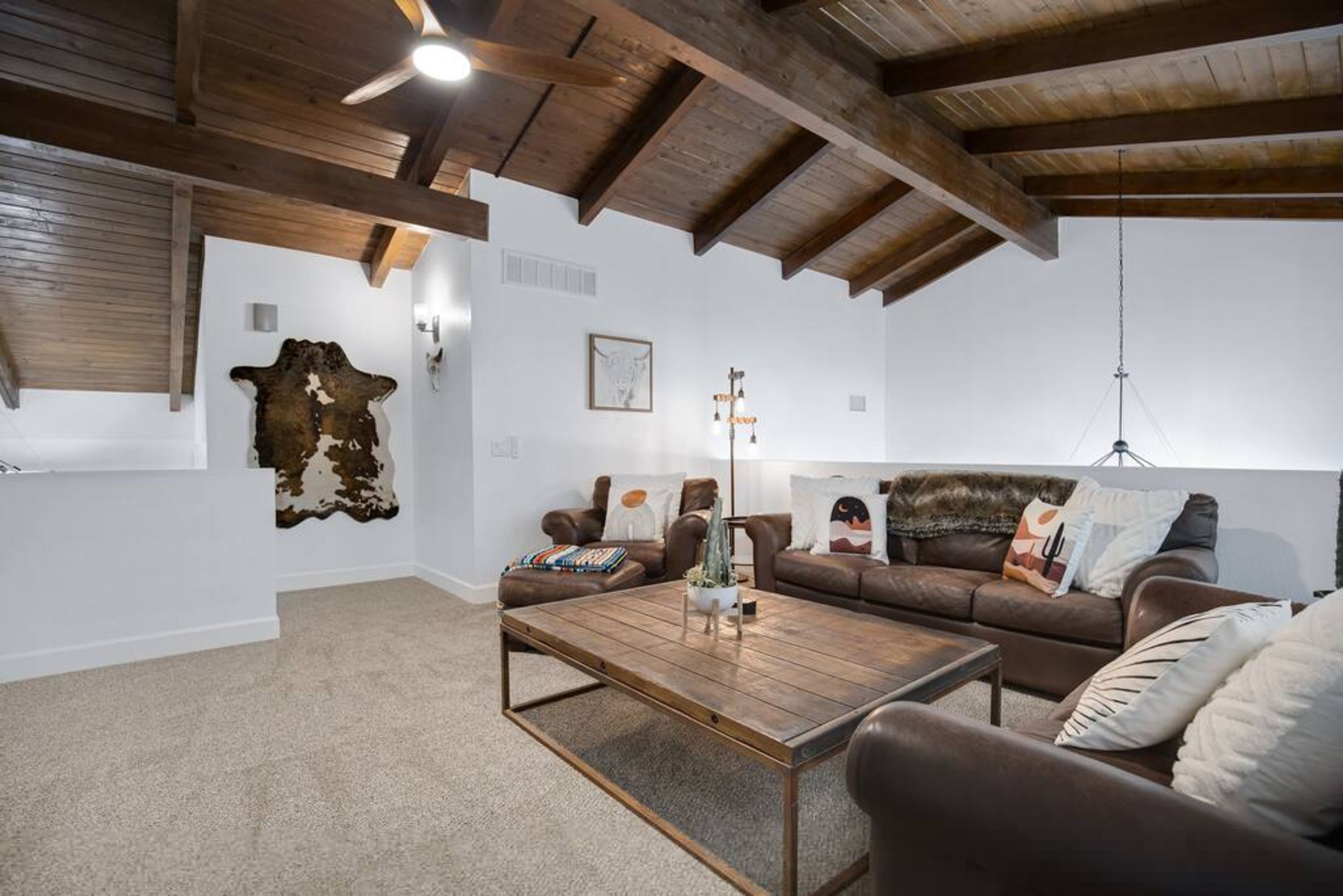 Ein gemütliches Wohnzimmer mit Holzbalkendecke, einem Ledersofa, einem Couchtisch und einem Wandbild aus Tierfell.