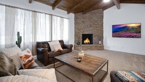 Uma sala de estar com lareira de pedra, sofá de couro, mesa de centro de madeira e uma grande pintura na parede.