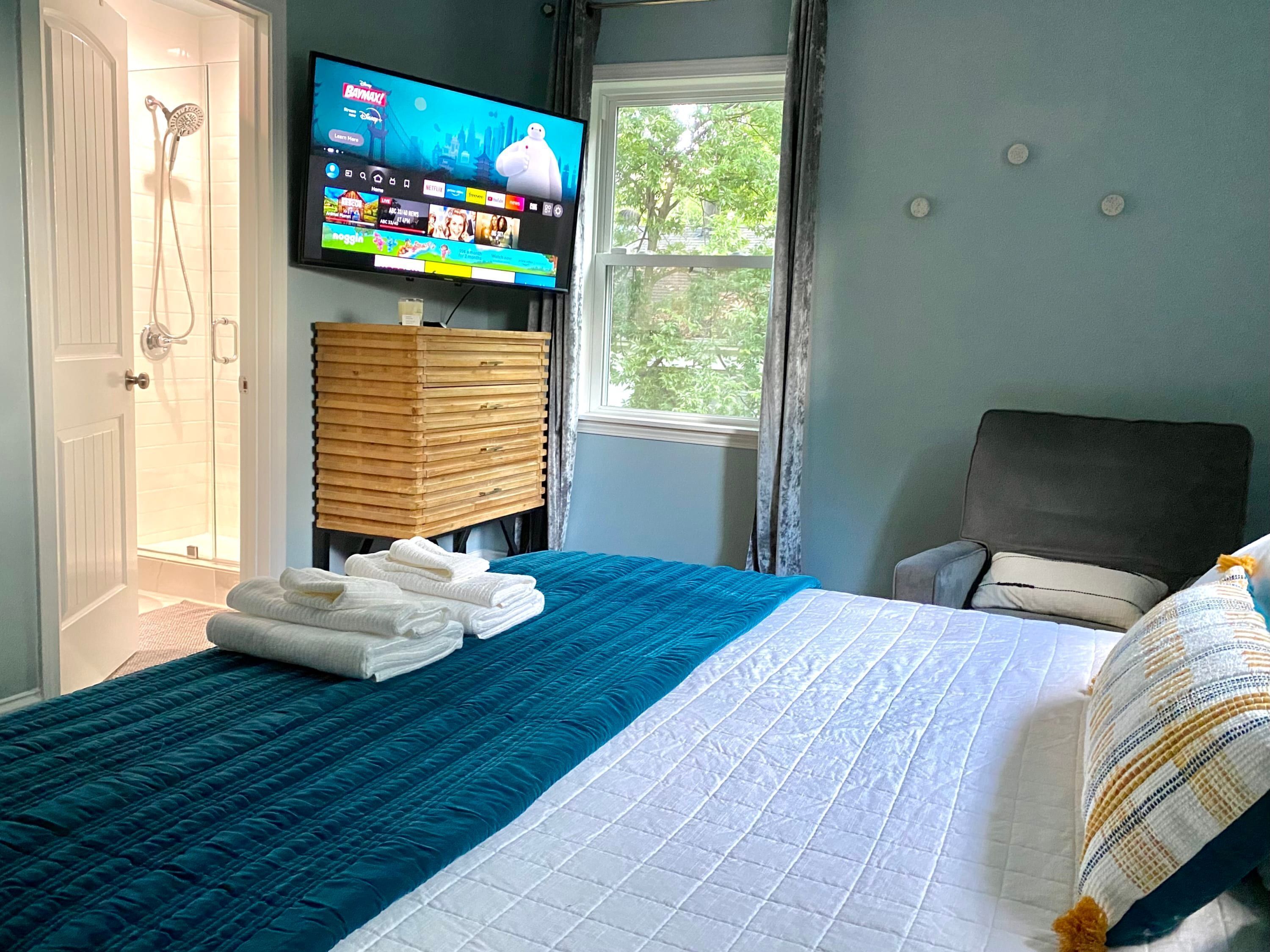 A hotel room with a bed, a TV mounted on the wall, a window, and a wooden cabinet.