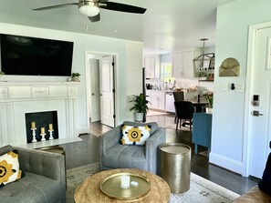 Un salon avec une cheminée, un téléviseur et un coin repas, avec une cuisine en arrière-plan.