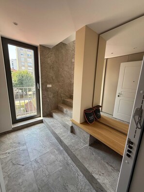 A modern bathroom with a marble floor, a wooden bench, a white door, and a view of a building outside through a glass door. - Crown Residence Luxury 2BR in Ljubljana Downtown (Ljubljana)