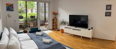 Un dormitorio moderno con cama, televisor y puerta corrediza de vidrio que da a un espacio exterior.