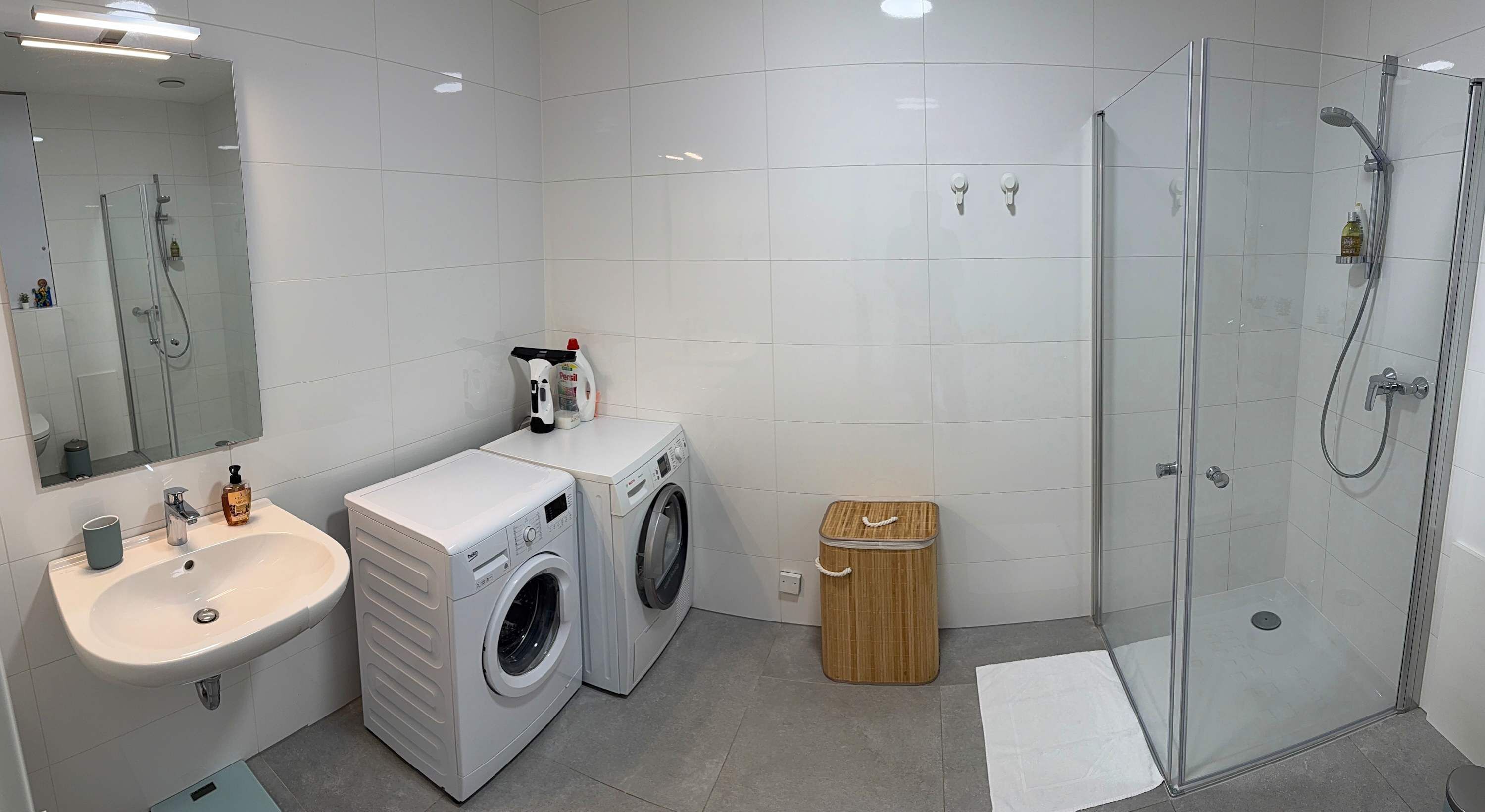 A modern bathroom with a sink, washing machine, and shower.