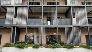 Een meerlaags gebouw met balkons, een betonnen basis en een verhard terrein.
