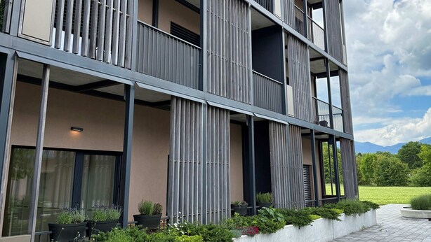 Een modern meerlaags gebouw met balkons, grote ramen en een aangelegde groene ruimte met planten.