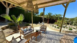 An outdoor patio with a thatched roof, wooden furniture, and a pool. - 3 Bedroom Villa Walking Distance to Moraira (Teulada)