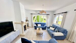 A living room with a TV, fireplace, blue sofas, and a coffee table. - 3 Bedroom Villa Walking Distance to Moraira (Teulada)