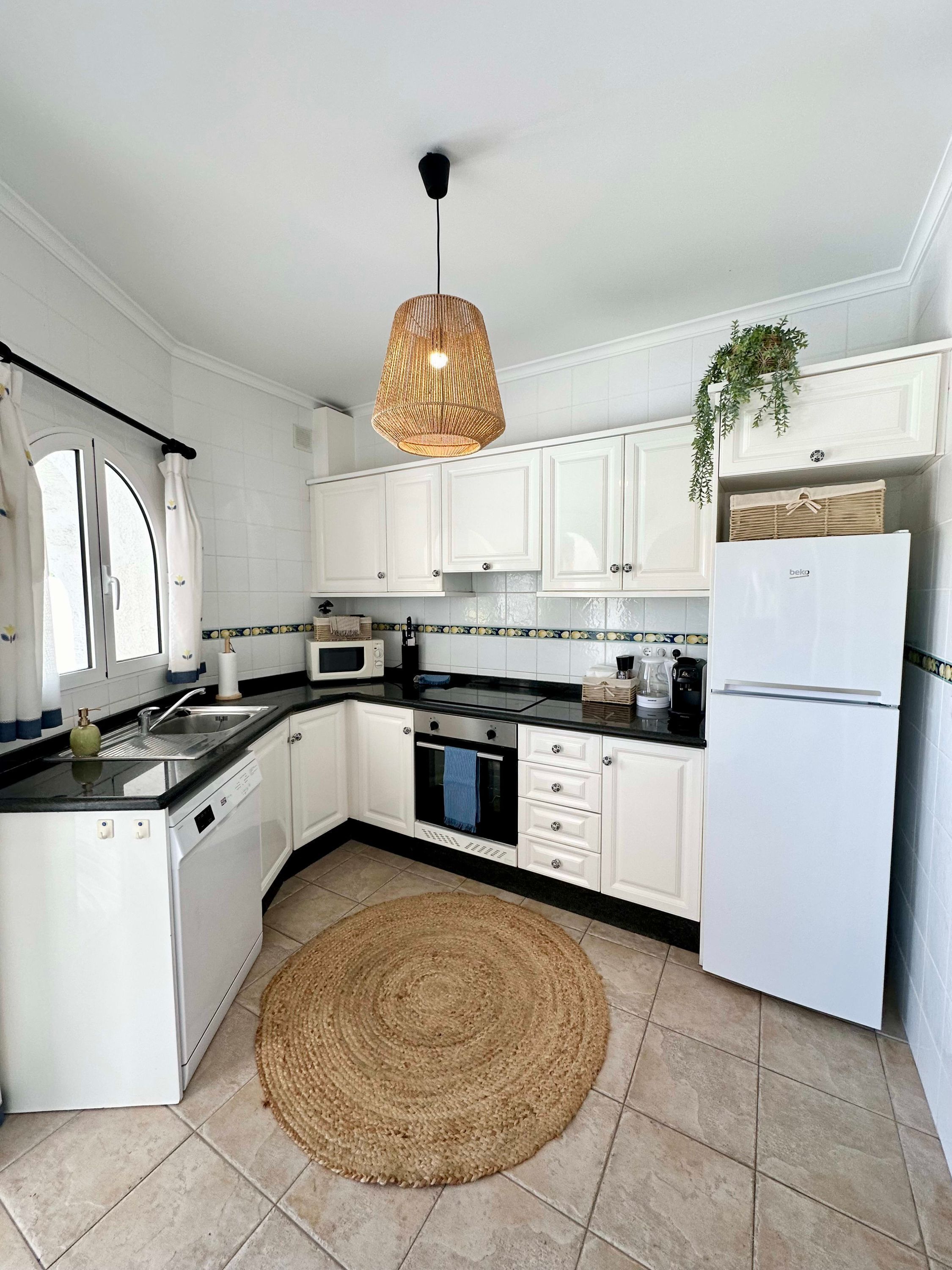 A modern kitchen with white cabinets, a black countertop, a built-in oven, a microwave, and a refrigerator.