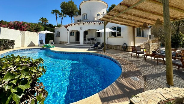 A poolside area with a clear blue pool, a covered patio with outdoor furniture, and a white building with arched windows. - 3 Bedroom Villa Walking Distance to Moraira (Teulada)