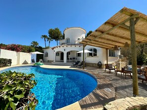 A poolside area with a clear blue pool, a covered patio with outdoor furniture, and a white building with arched windows. - 3 Bedroom Villa Walking Distance to Moraira (Teulada)