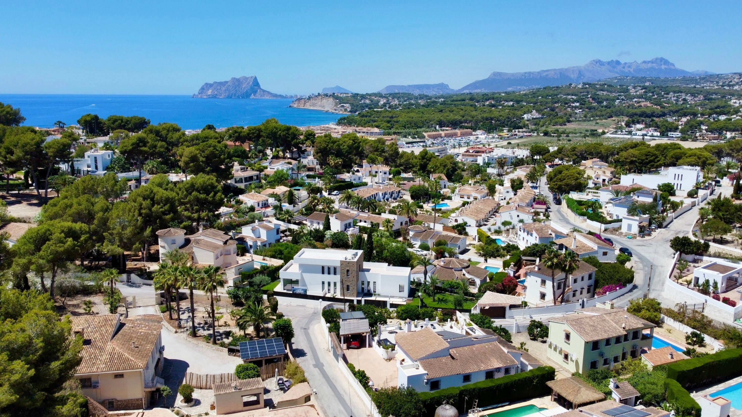 Una zona residenziale costiera con case, un mare blu limpido e montagne sullo sfondo.