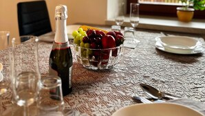 A dining table with a bottle of wine, a bowl of fruit, and a view of mountains through a window.