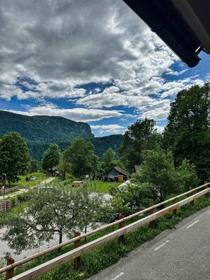 A rural landscape with a road, wooden fence, and a small building surrounded by trees and hills. - Bijol Apartments - 1-bedroom Apartment K (Bled)